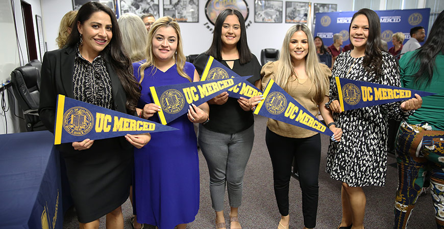 A group of people hold up UC Merced pennants.