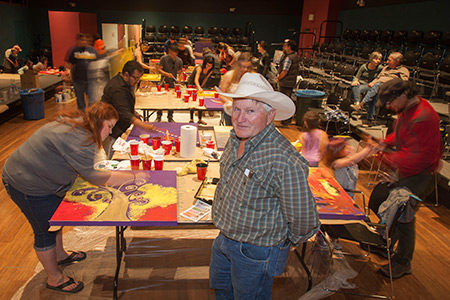 Artist Dwight Wigley stands in front of a group of community members as they paint their portions of an art installation.