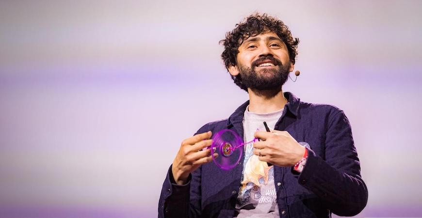 A man holds a bright purple instrument in his hands while talking into a microphone headset. 