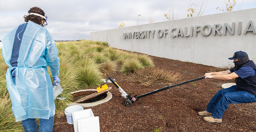 Professor Marc Beutel waits to collect a wastewater sample as a facilities employee helps to remove the manhole covering on campus.